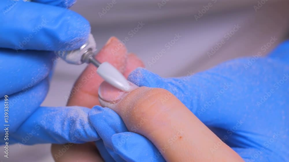 The master uses an electric machine to remove the nail polish on client hands during hardware manicure in the salon. Beauty and nail care concept The master uses an electric machine to remove the nail polish on client hands during hardware manicure in the salon. Beauty and nail care concept