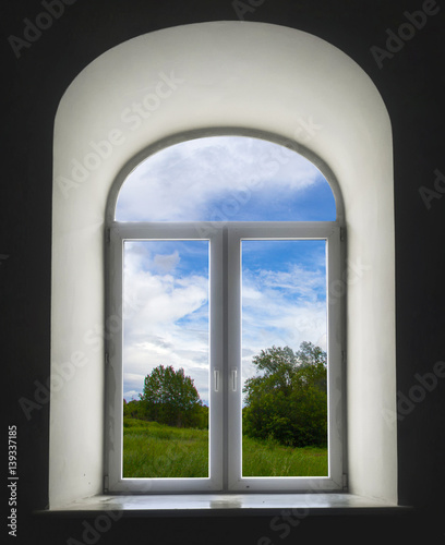 white semicircular modernist windows on a black wall.summer  sky  clouds  trees  grass  meadow in the window