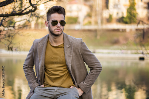 Handsome young man sitting in front of river in a city, looking confident and relaxed