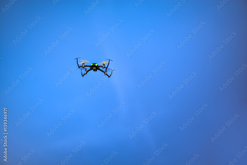Black, small, mini quadrocopter flying high in the air, taking photos, recording footage from above. Flying drone with four motors, yellow propellers, camera on clear blue sky background. Surveillance Black, small, mini quadrocopter flying high in the air, taking photos, recording footage from above. Flying drone with four motors, yellow propellers, camera on clear blue sky background. Surveillance