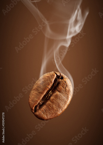 Closeup falling coffee bean with smoke on brown background