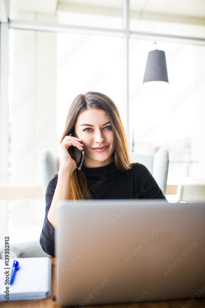 Freelance young smile woman sitting in the cafeteria with laptop and using mobile phone Freelance young smile woman sitting in the cafeteria with laptop and using mobile phone