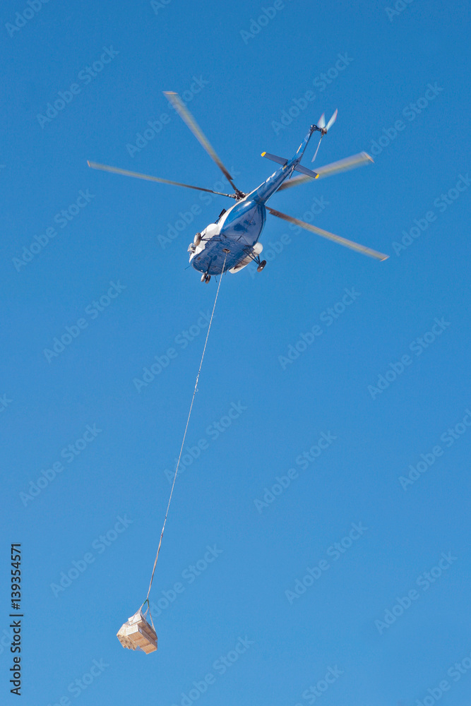 The helicopter carries cargo against blue sky
