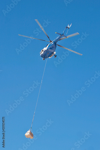 The helicopter carries cargo against blue sky 