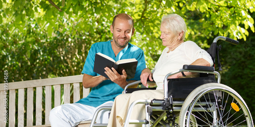 Obraz na płótnie Carer reads a book to the elderly persons