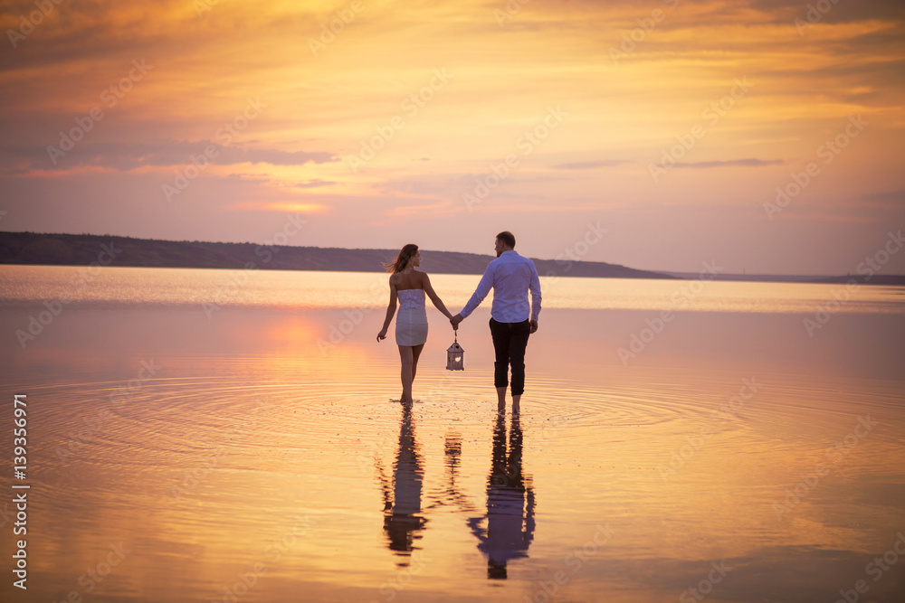 Couple in love at lake orange sunset, walking in water