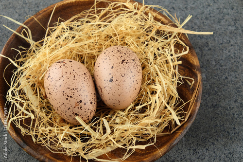 Two quail easter eggs on wooden plate with hay.