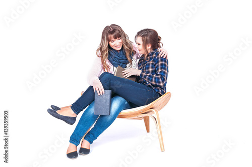 Full length portrait of two siting beautiful weman students holding books isolated on a white background