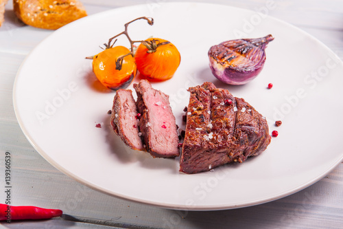 Close up Grilled beef tenderloin steak with grilled onion and cherry tomatoes on the white plate on the wooden background with details. Selective focus