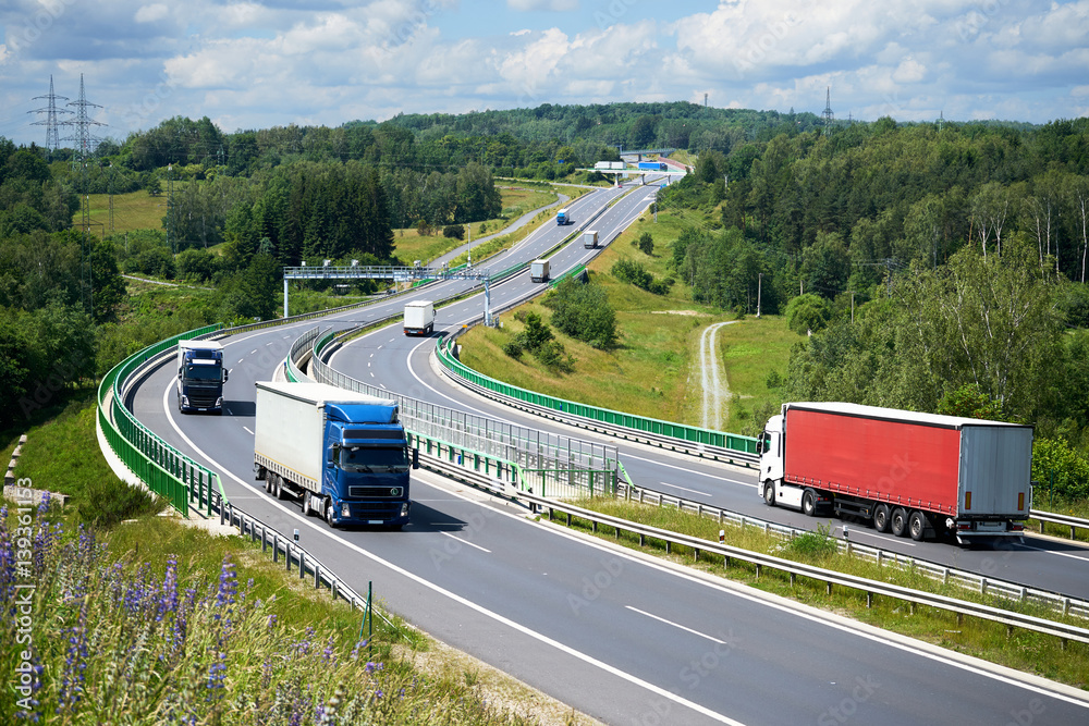 View from above of trucks driving on the highway with electronic toll gates in a wooded landscape.