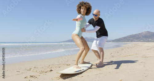 Tableau sur toile The instructor teaching the female beginner surfer standing on a surfboard in Tarifa beach