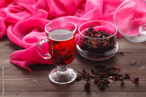 Transparent cup of Hibiscus tea on a background of dry tea