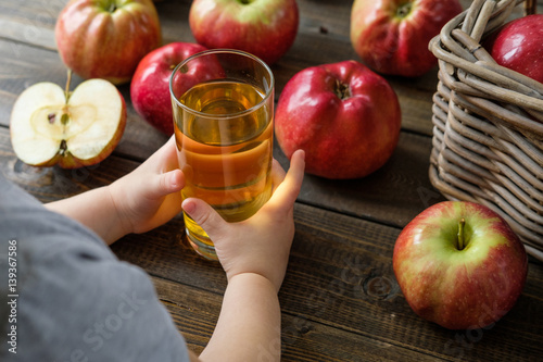 a glass of juice in children's hands on a background of red ripe apples