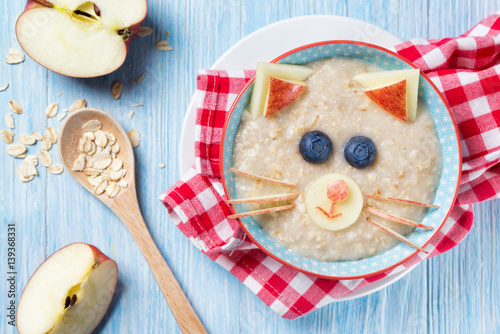 Funny oat porridge with cat, kitten face made of fruit and berries, food for kids idea, top view