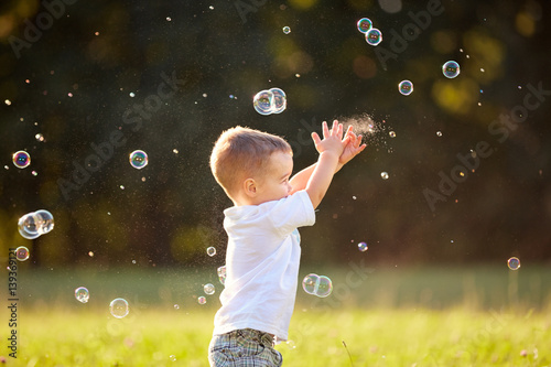 Kid in nature reaching soap bubbles