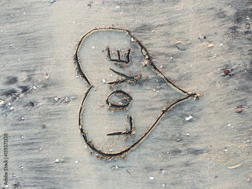 Love written inside a heart shape, in sand on a beach