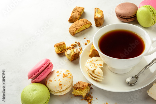 Cup of black tea with tasty almond cookies rich in vitamins minerals and varicolored macaroons on a white background in light key. Copy space.