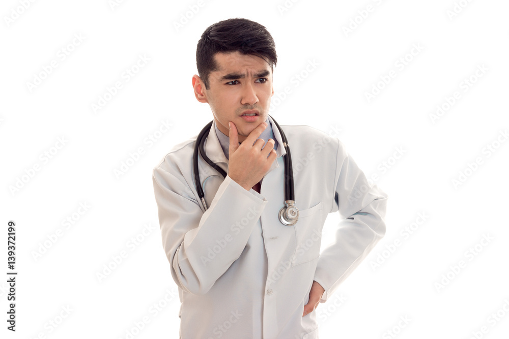 a young doctor in a white lab coat with a stethoscope thoughtfully looks toward a young doctor in a white lab coat with a stethoscope thoughtfully looks toward
