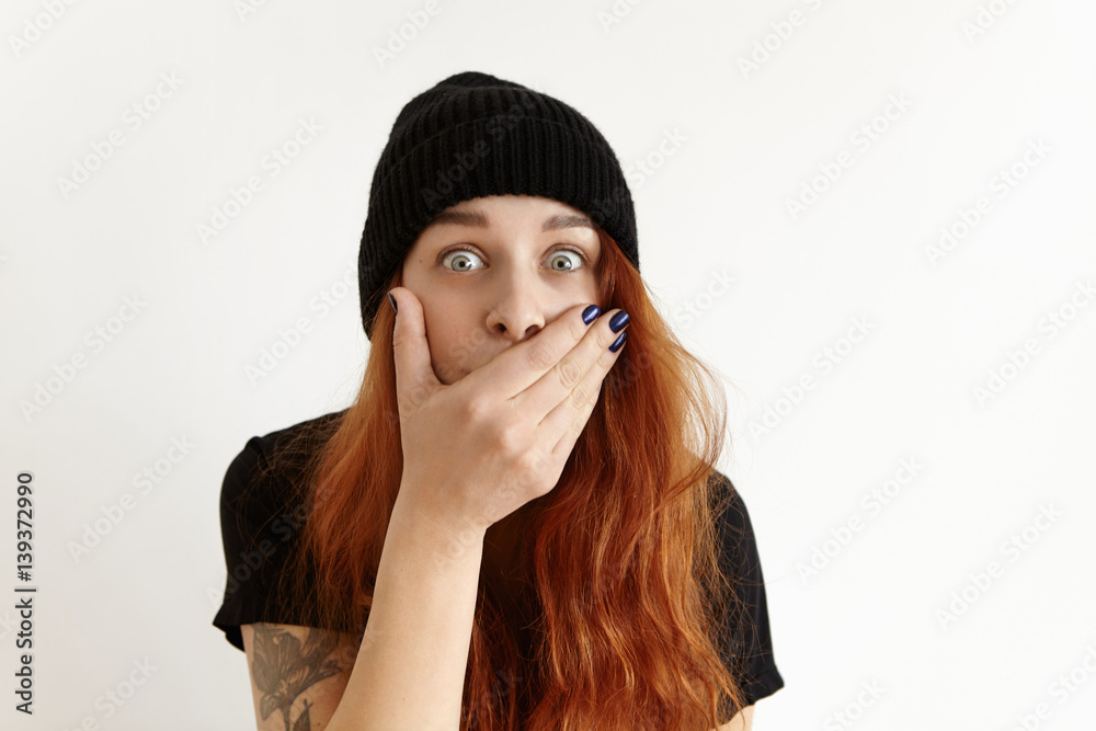 Omg! Surprised funny goggle-eyed redhead girl in stylish black clothes covering mouth with hand, looking at camera in astonishment, shocked with some astonishing news or gossip. Body language Omg! Surprised funny goggle-eyed redhead girl in stylish black clothes covering mouth with hand, looking at camera in astonishment, shocked with some astonishing news or gossip. Body language