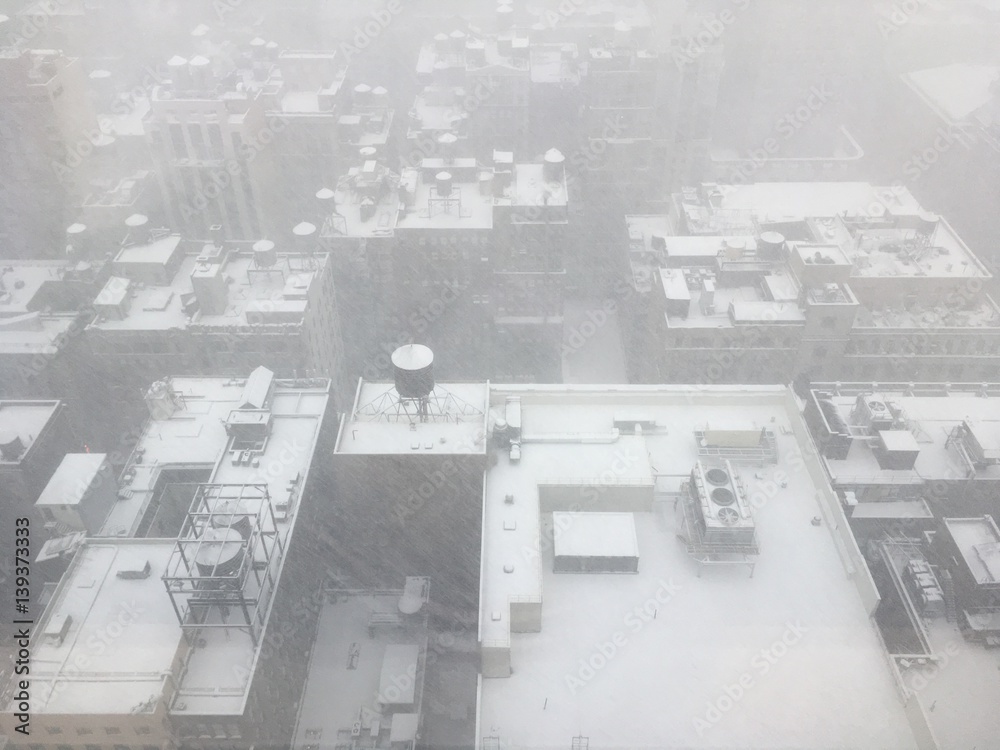 Looking out of a skyscraper window down on the snow-covered roofs below, Water tanks, air conditioning units, and rooftops covered in snow in Midtown Manhattan, NY.
