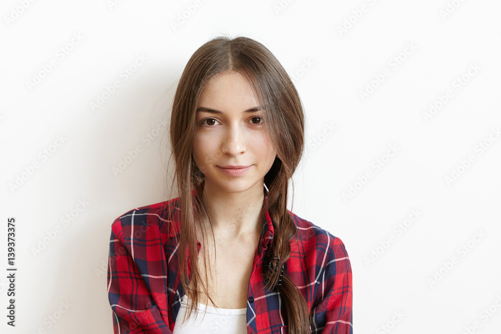 People, lesiure and lifestyle concept. Beautiful and charming young Caucasian female with brown eyes and messy dark hair in braid sitting alone at white blank wall, wearing red checkered shirt People, lesiure and lifestyle concept. Beautiful and charming young Caucasian female with brown eyes and messy dark hair in braid sitting alone at white blank wall, wearing red checkered shirt