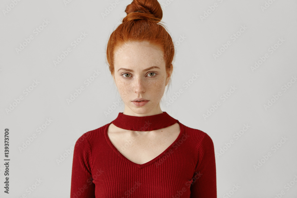 Beauty, style, fashion, clothing and design concept. Gorgeous luxurious Caucasian redhead woman with hair bun and freckles wearing stylish red dress with geometrical cut out before going out on date - obrazy, fototapety, plakaty 
