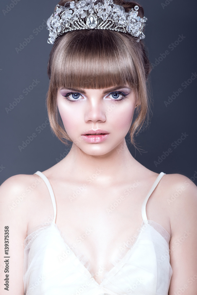 Fototapeta premium Portrait of young beautiful teenager girl with expressive blue eyes and full parted lips wearing jewel crystal crown looking straight ahead. Isolated on grey background. Close up. Studio shot