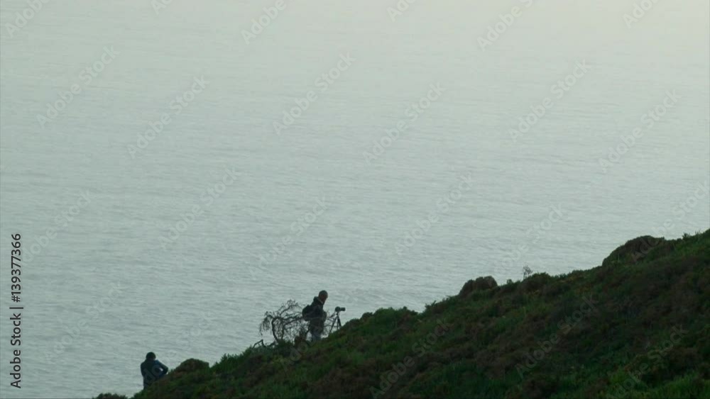 Tourist man and a photographer on a mountain cliff ocean coast, beautiful water landscape Tourist man and a photographer on a mountain cliff ocean coast, beautiful water landscape
