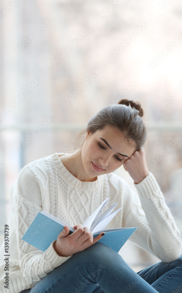 Obraz premium Young woman reading book on windowsill at home