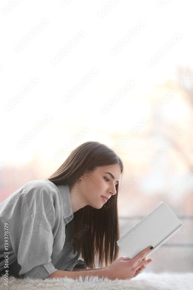 Obraz premium Young woman reading book on windowsill at home
