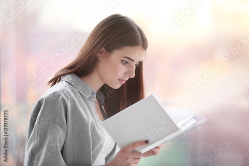 Young woman reading book on windowsill at home