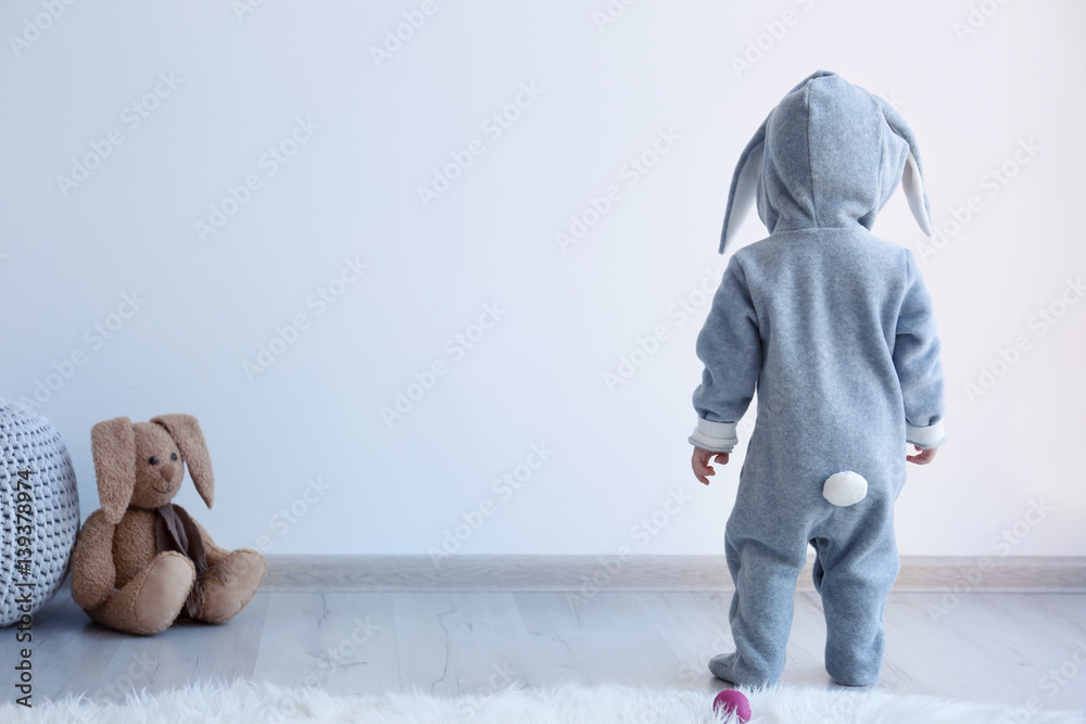 Cute little child in bunny costume standing at home - obrazy, fototapety, plakaty 