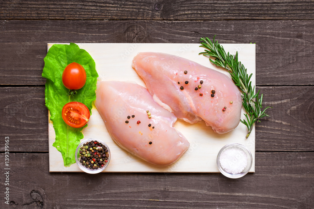 Raw chicken breast fillets on wooden cutting board with vegetables Raw chicken breast fillets on wooden cutting board with vegetables