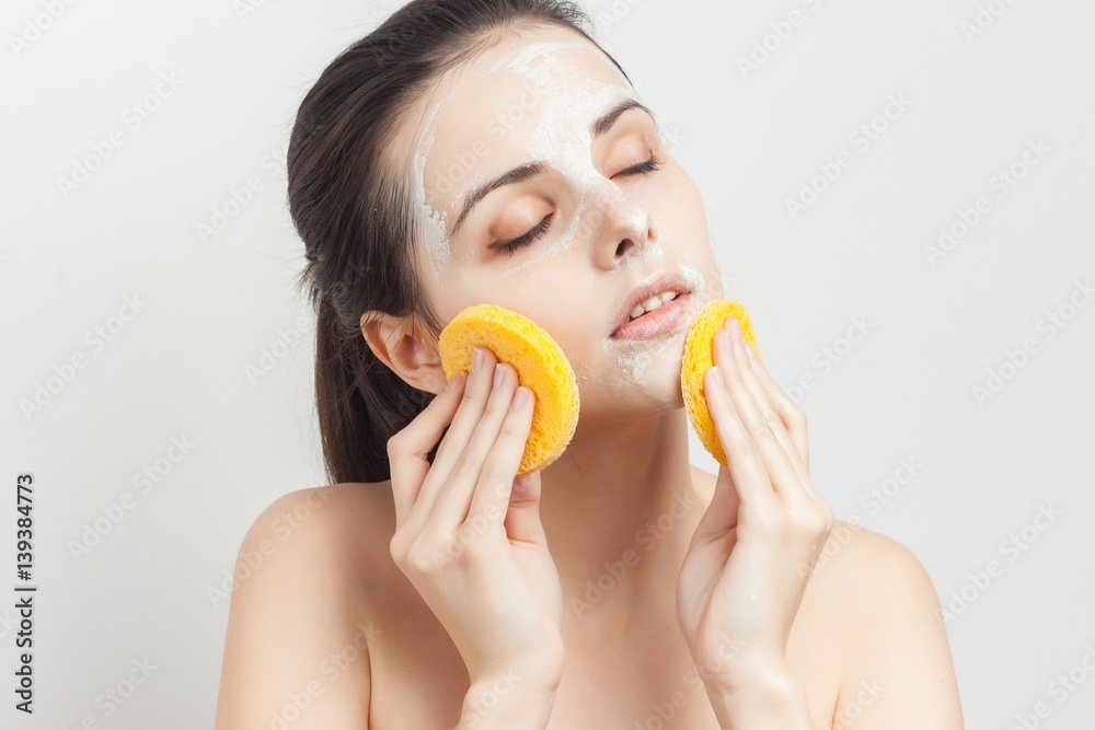 a woman wipes her face with yellow sponges, a white mask, closed eyes a woman wipes her face with yellow sponges, a white mask, closed eyes