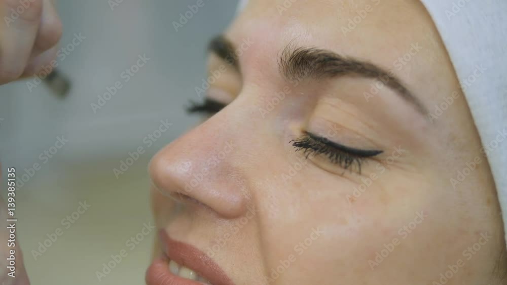 Closeup of beautician hands using tweezers on woman's eyebrow at beauty salon Closeup of beautician hands using tweezers on woman's eyebrow at beauty salon