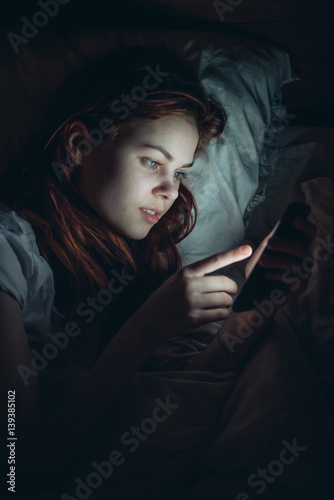woman lies in bed and phone in hand