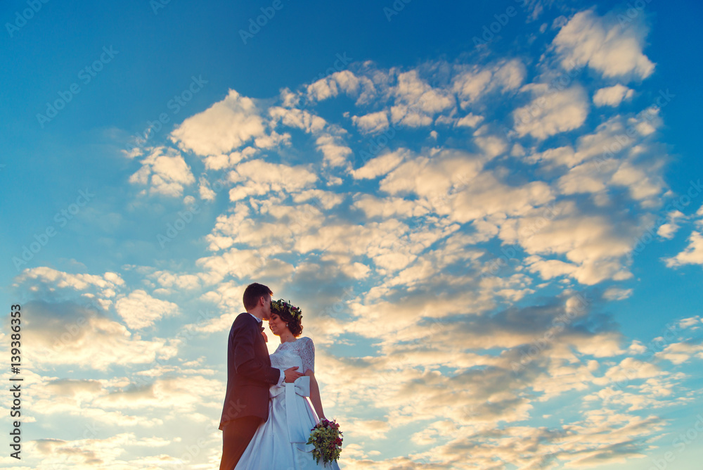 Loving adorable couple standing together against the sky at sunset