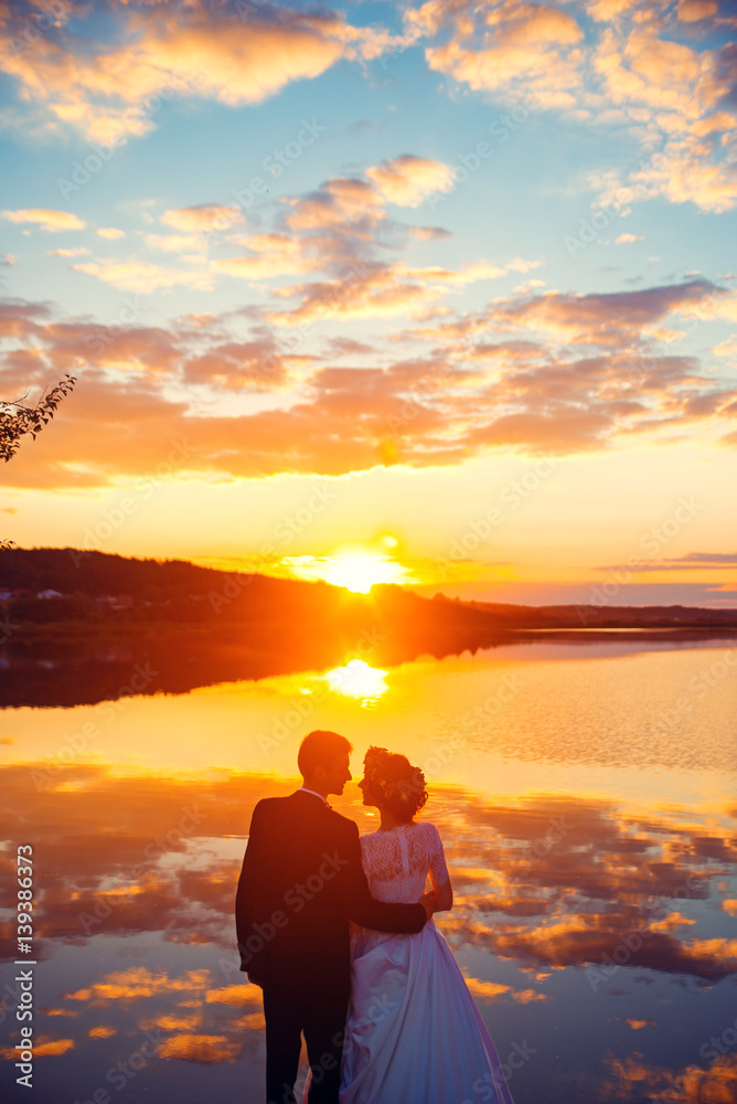 Loving attractive couple standing together on the background of the lake at sunset