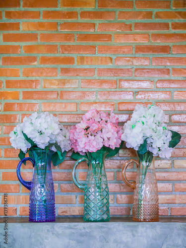 White and pink artificial flowers in vases on red brick wall background. Blue, green and orange vases.