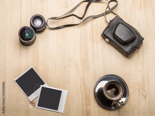 photo camera, photo frames, lenses, cup of coffee on wooden table around copy space in center, top view, flat lay