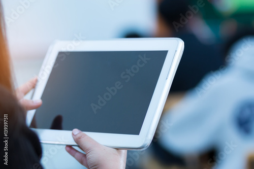 teacher hand holding use tablet with blurred student in classroom background, education concept