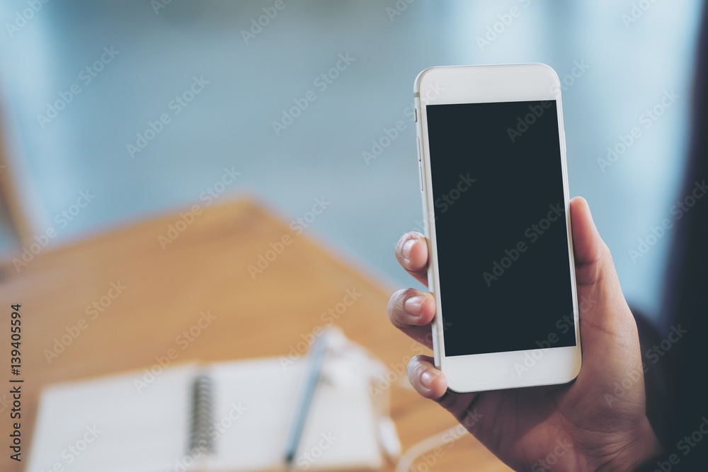 Mockup image of hands holding white mobile phone with blank white screen on vintage wooden room Mockup image of hands holding white mobile phone with blank white screen on vintage wooden room