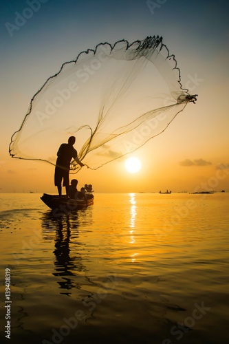Silhouettes fisherman throwing fishing nets during sunset, Thailand. photo