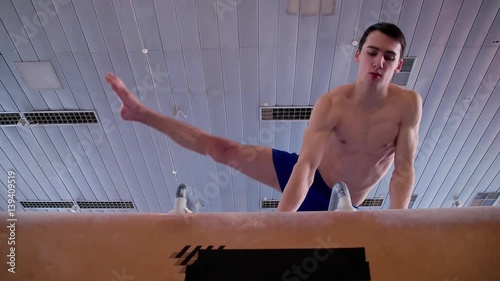 Young gymnast doing routine exercises on pommel horse HD slow-motion video. Olympics athlete training gymnastics skills: circles flairs trick performing, swings turning motion