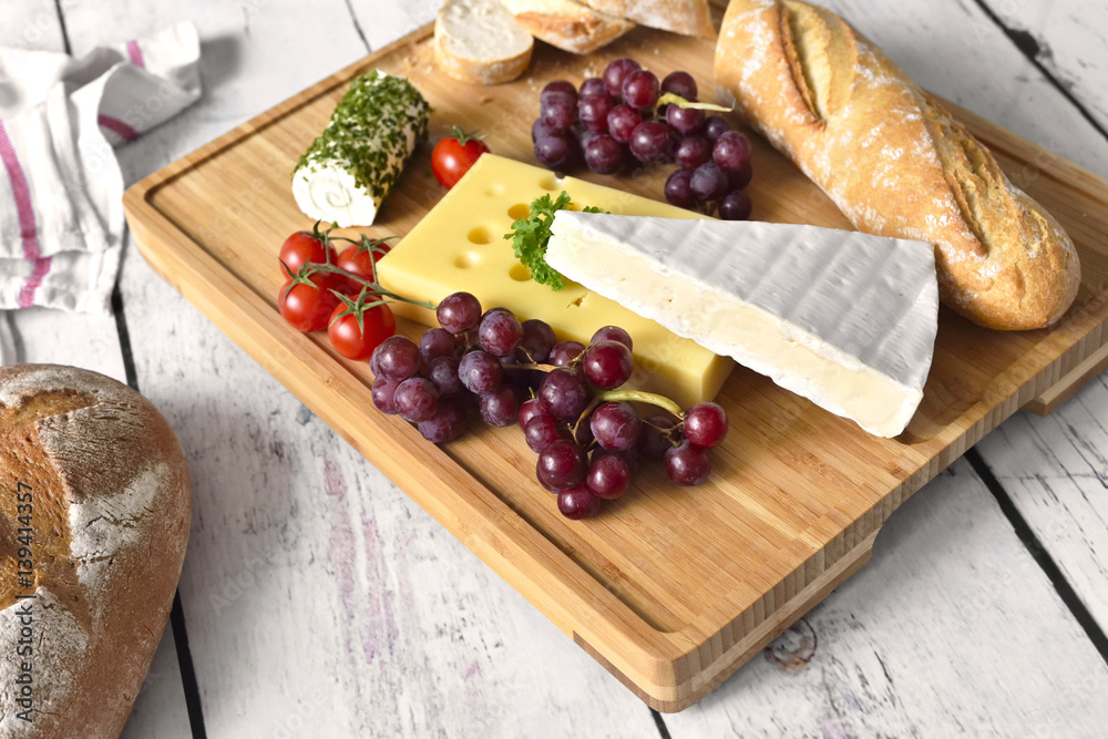 Healthy eating scene of a cheese plate with fresh baguette, fresh tomatoes and fruits. Wooden table, rustic scene. Healthy eating scene of a cheese plate with fresh baguette, fresh tomatoes and fruits. Wooden table, rustic scene.