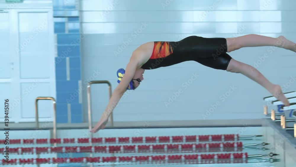 Female swimmer jumps off starting block and start swims in pool HD slow-motion video. Professional athlete training: dive and splashes water surface