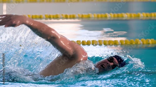 Male swimmer swims in pool HD slow-motion video. Front crawl freestyle training of professional man athlete. Water splashing of arms stroke. Side view