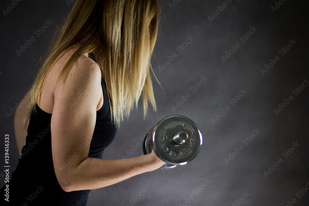 Fototapeta premium Young woman doing exercise with dumbbells, over black