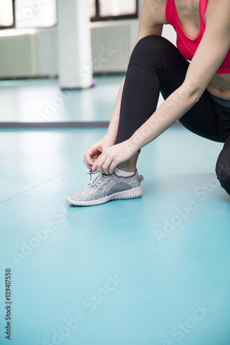 Young woman ties the laces on the shoes in the gym