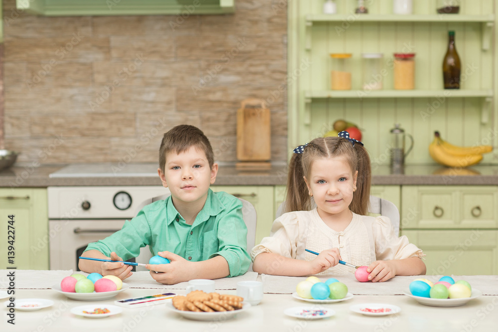 Cute brother and sister draw on the Easter eggs at the table.and laugh Cute brother and sister draw on the Easter eggs at the table.and laugh